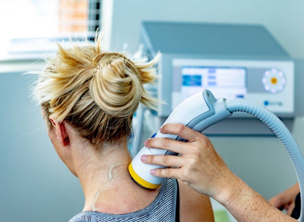 A person receiving a laser treatment on the neck with a handheld device in a clinical setting.