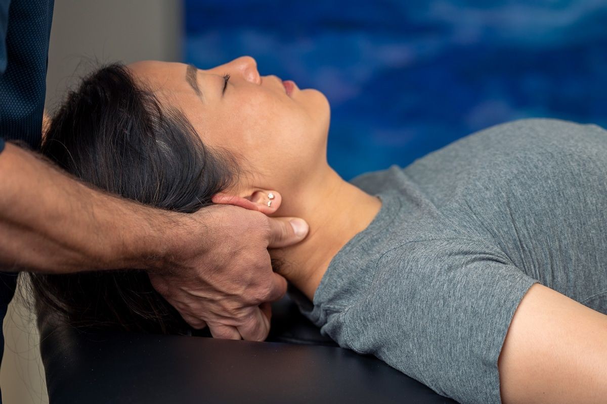 A woman lying down receiving a neck massage from a therapist's hand.